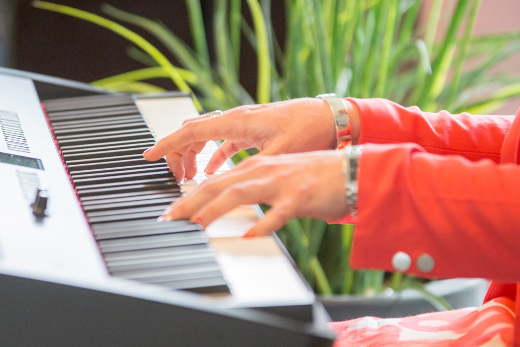 Man sieht Tinas Hände auf dem E-Piano während sie auf der Hochzeit ihrer besten Freundin als Wedding-Singer auftritt. Sie trägt silberne Armbänder, ein Kleid und einen Blaser, da sie die Trauzeugin ist.