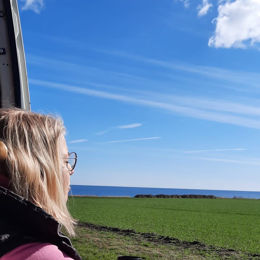 Tina Niemann sitzt in der geöffneten Tür des ausgebauten Crafters und genießt mit geschlossenen Augen die Natur. Der Stellplatz befindet sich in unmittelbarer Nähe zum Meer.