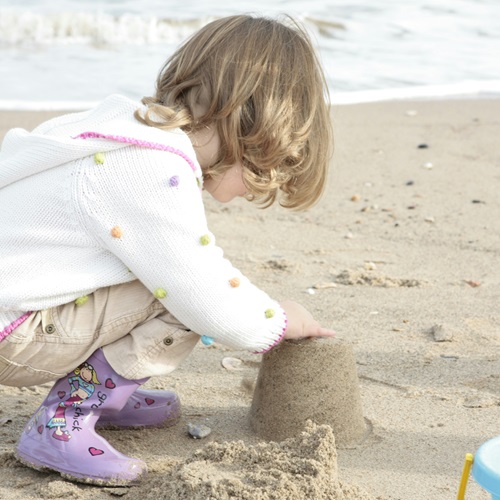 Ein Kind sitzt am Strand und baut im Sand einen Sandburg