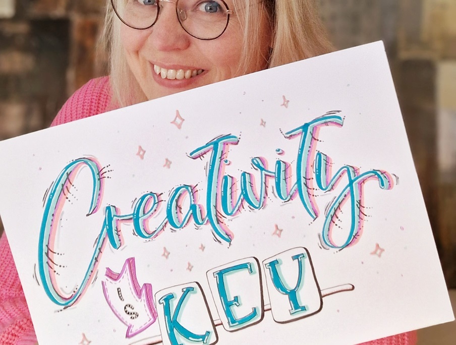 Tina hält ihr Handlettering-Werk mit den Worten "Creativity is key" in die Kamera. Sie bezieht sich darauf, dass Kreativität eine Schlüsselkompetenz in der heutigen Gesellschaft ist.