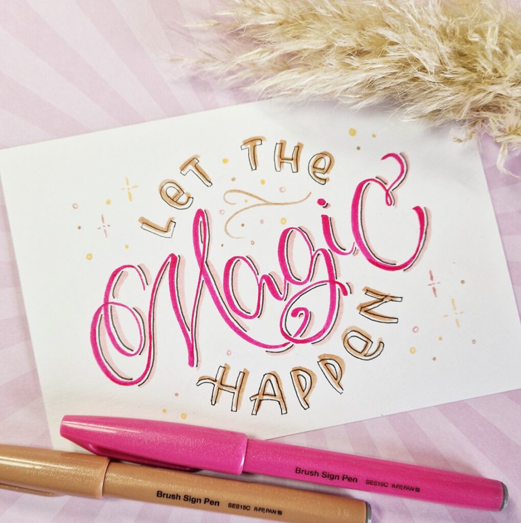 Das Foto zeigt ein Handlettering mit den Worten "Let the Magic Happen" im Flourishing Letters Stil. Es sind die Pentel Sign Pen Brush zu sehen.