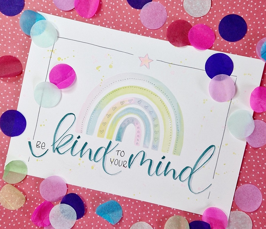 Das Bild zeigt einen Aquarell Regenbogen mit dem Handlettering Spruch "Be kind to your mind" und Konfetti drumherum