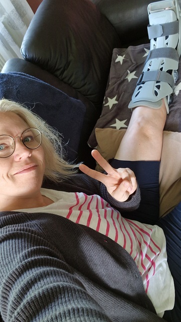 Tina sitzt auf der Couch, am linken Bein eine Beinschiene zum Schutz des gebrochenen Knochens