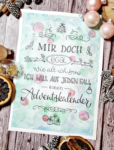 Das Bild zeigt ein Lettering mit dem Text "Ist mir egal, wie alt ich bin - ich will auf jeden Fall einen Adventskalender". Es ist mit weihnachtlichen Doodles verziert und liegt auf einer weihnachtlich dekorierten Tischplatte.