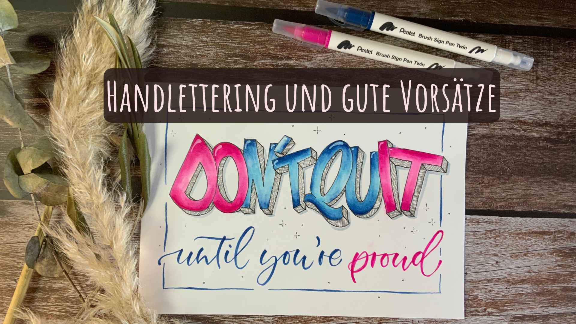 Das Bild zeigt ein Lettering mit den Worten "Don't quit until you're proud". Auf dem Tisch liegt ein wenig getrocknete Deko und zwei Brush-Pens